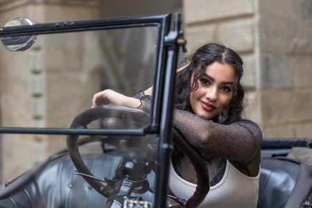 Attractive young woman with long black hair is posing on vintage car. Horizontally.の写真素材
