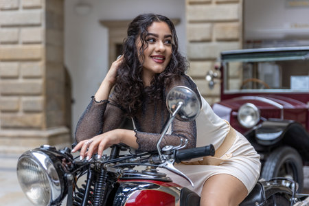 Attractive young woman with long black hair is sitting in a sexy pose on  vintage motorcycle. Horizontally.の写真素材