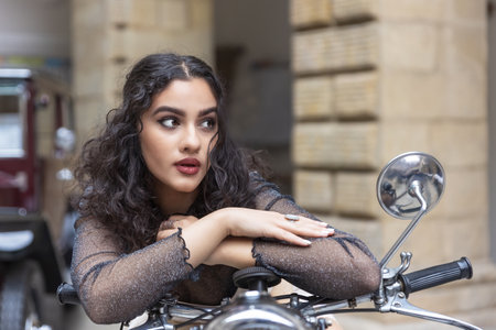 Sexy black hair tanned girl with red lips is posing on a vintage motorcycle. Horizontally.の写真素材