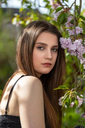 Cool brunette girl posing on camera outdoors near sakura tree. Vertically.の写真素材
