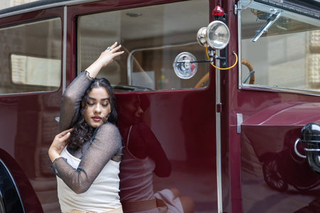 Tanned black hair girl is posing on red vintage car with closed eyes. Horizontally.の写真素材