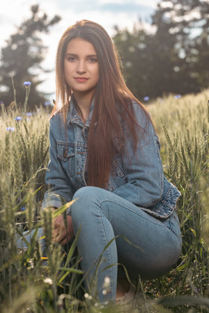 Atractive long haired  brunette girl dressed in jeans is posing in a cereal field. Vertically.の写真素材