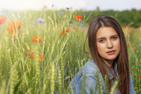 Beautiful brunette girl is posing in  cereal field. Red poppies and blue  cornflowers in the sunlight are in the background.の写真素材