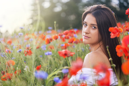 Closeup side profile view of cool brunette girl exposing her shoulder sitting in red poppies and blue cornflowers  meadow.の写真素材