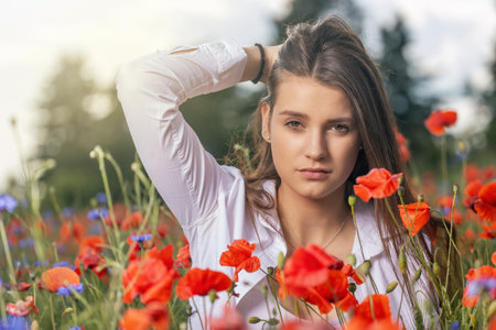 Atractive brunette girl with hand in her hair is posing in a red poppies field. Horizontally.の写真素材