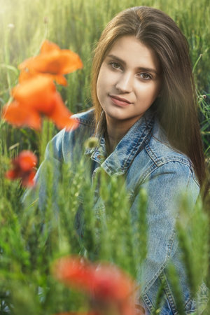 Closeup portrait of beautiful long haired brunette tanned girl dressed in jeans sitting in cornfield.  Vertically.の写真素材