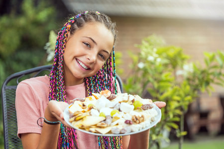 Little smiling long haired girl is holding a plate full of cheeses outdoors.  Horizontally.の写真素材