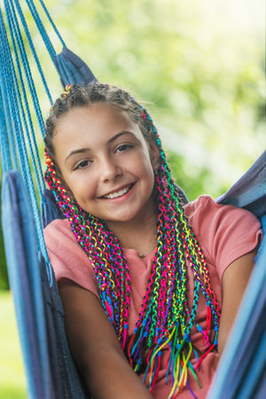 Laughing young girl with colorful braids in her hair is posing on hammock. Vertically.の写真素材