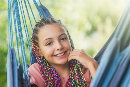 Closeup portrait of laughing young girl with colorful braids in her hair posing on blue hammock.  Horizontally.の写真素材