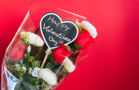 Bouquet of red and white roses, with a blackboard heart with the message "Happy Valentine's Day" written in chalk, against a red background.の写真素材
