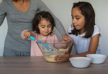 Mother and her two daughters prepare some cookies with chocolate in their kitchen.の写真素材