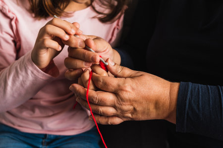 Grandmother teaching her granddaughter to knit with needle, both sitting on the sofa in the living room at home.の写真素材