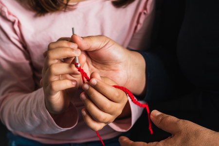 Grandmother teaching her granddaughter to knit with needle, both sitting on the sofa in the living room at home.の写真素材