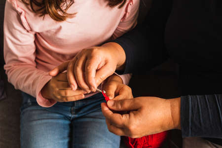 Grandmother teaching her granddaughter to knit with needle, both sitting on the sofa in the living room at home.の写真素材