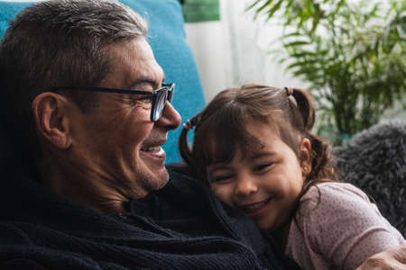 Granddaughter on her grandfather's chest, the two of them lying on the sofa at home, very happy to be together.の写真素材