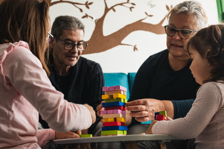 Grandmother and grandfather playing a board game with their two granddaughters, all Caucasian, sitting in the living room, smiling while having a great time together.の写真素材