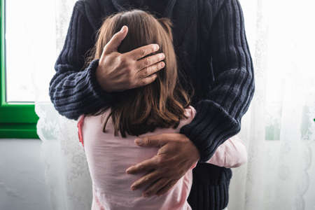 Grandfather sadly hugs his granddaughter who is crying inconsolably, to calm her discomfort.の写真素材