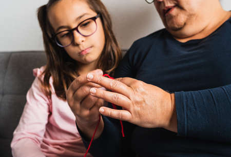 Grandmother teaching her granddaughter to knit with needle, both sitting on the sofa in the living room at home.の写真素材
