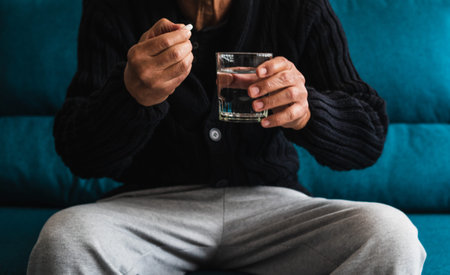 An elderly Caucasian man takes a medication from a container in his living room to combat his...
