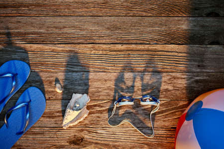 a beach ball sandals shells and swimming goggles on a dock at sunsetの写真素材