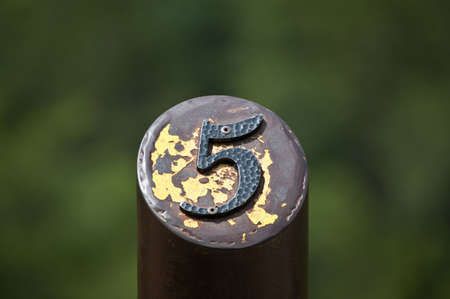 A number 5 on the top of a rusting metal post with peeling yellow paint.の写真素材