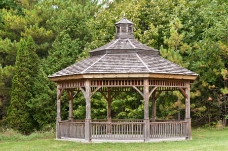A wooden gazebo stands in front of some green trees in a park.の写真素材