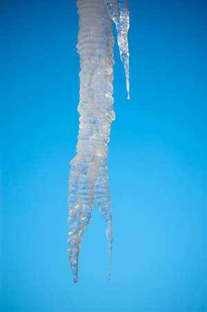 The sun shines through a large icicle with the blue sky in the background.の写真素材