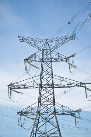 A transmission tower carrying high-voltage electrical lines stands against a blue sky.