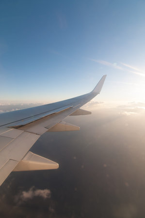 The right wing of a flying airliner with blue sky and clouds.の写真素材