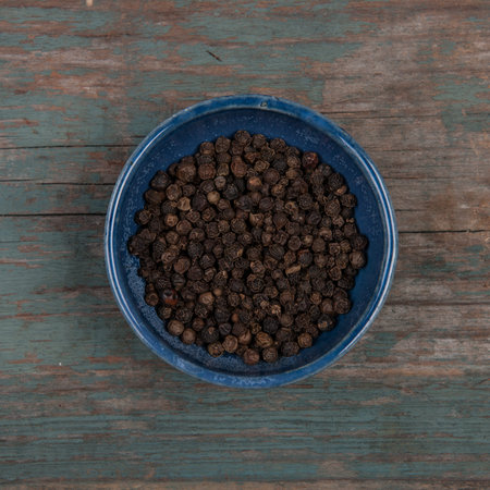Small bowl of pepper corns, on a wooden table
