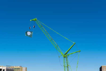 Green crane on a beautiful blue sky. The crane has a white and green flag at the tip, waving in the wind. It is a beautiful sunny spring day.の写真素材