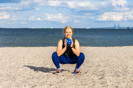 Young caucasian woman doing gym exercises and training on the beach in Amager, Copenhagen, Denmark. The girl is training with a kettle ball. It is a sunny spring evening.の写真素材