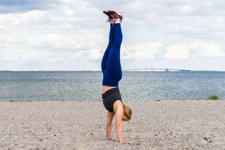 Young caucasian woman doing gym exercises and training on the beach in Amager, Copenhagen, Denmark. The girl is doing a handstand. It is a sunny spring evening.の写真素材