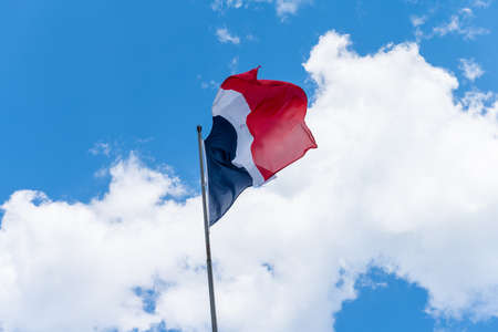 The red, blue and white French flag waving in the wind. It is a beautiful sunny summer day, with blue sky and white clouds.の写真素材