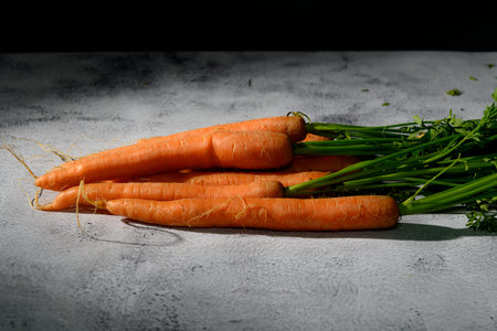 Ripe, fresh orange carrots with top, lying on a rustic kitchen table.