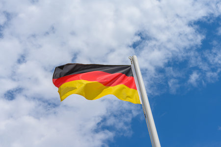 German flag waving in the wind. It is a beautiful sunny summer day, with blue sky and white clouds in the background.の写真素材