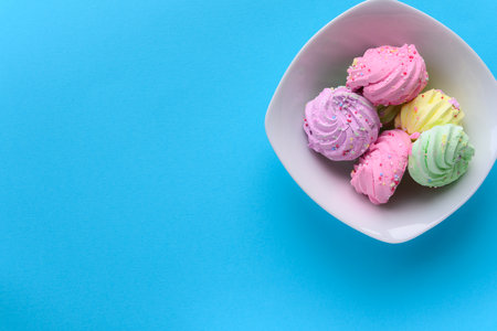 Very colorful meringues placed in a white bowl, on a light blue background. Pastel green, purple, pink and yellow colors with sprinkles on them. Copy space on left side.の写真素材