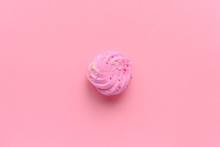 Still life of a very colorful meringues, with colored sprinkles on, placed on a pink background. A single meringue is lying in the middle of the frame. Plenty of copy space around.の写真素材