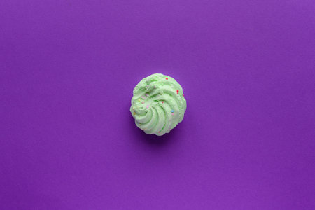 Still life of a very colorful meringues, with colored sprinkles on, placed on a purple background. A single green meringue is lying in the middle of the frame. Plenty of copy space around.の写真素材