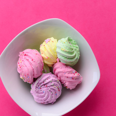 Very colorful meringues placed in a white bowl, on a pink background. Pastel green, purple, pink and yellow colors with sprinkles on them. Little copy space on right side and topの写真素材