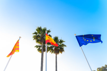 EU, Spain and local Ibiza flags waving gently in the wind, at the Cala San Vicente beach in Ibiza, Spain. It is a beautiful sunny summer day with a clear blue sky in the background.の写真素材