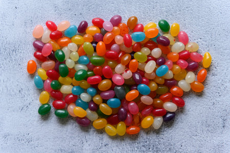 Big round pile of very colorful jellybean sweets placed in the middle of the frame, on a rustic grey background. Delicious looking candy in strong, saturated colors.の写真素材