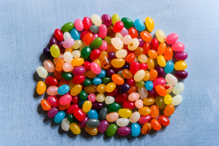 Big round pile of very colorful jellybean sweets placed in the middle of the frame, on a rustic grey background. Delicious looking candy in strong, saturated colors.の写真素材