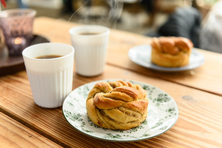 Two plates with a delicious cardamom bun on each, and two hot coffees on a table in a cafe. Steam is coming up from the cupsの写真素材