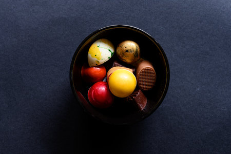 Small black round bowl with delicious homemade colorful chocolate in it. On a black background, with copy space around.の写真素材