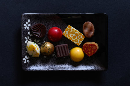 Small grey and black plate with delicious homemade colorful chocolate on it. On a black background, with copy space aroundの写真素材