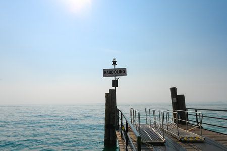 Landing bridge in Bardolino, Lake Garda, Italy, where the tourist ferries board and onboard passengers. It is a beautiful sunny summer day, with a bit of fog over the lakeの写真素材