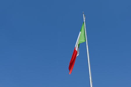 Italian flag gently waving in the wind, on a beautiful sunny summer day. There is a clear, blue sky in the background, without any cloudsの写真素材