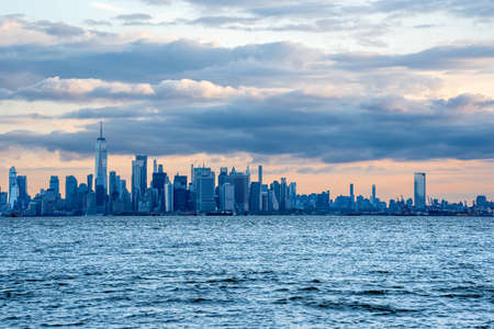 New York, NY - USA - April 10, 2022: horizontal image of the scenic New York Harbor and iconic Lower Manhattan. Seen during the sunrise with dramatic clouds and sky.のeditorial素材