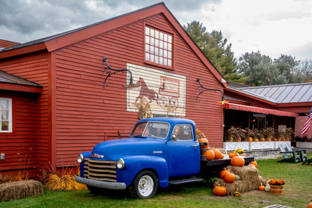 Weston, VT - USA - Oct. 7, 2022 Horizontal display of pumpkins, flowers, gourds and straw on a classic blue American pickup parked along the red wooden Vermont Country Store in quaint Weston.のeditorial素材